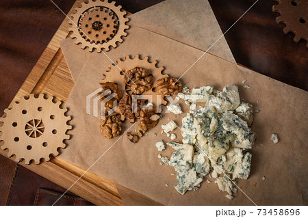 Top view of a blue cheese or bleu cheese served with walnuts on food wrapping paper and chalkboard with decorative wooden details of a simple mechanism. Cheese with the mold Top view of a blue cheese or bleu cheese served with walnuts on food wrapping paper and chalkboard with decorative wooden details of a simple mechanism. Cheese with the mold 73458696