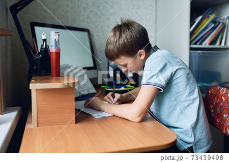 A boy is sitting at his desk and studying online 73459498