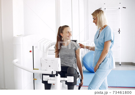 Young woman doing exercises on simulator with therapist in gym 73461800