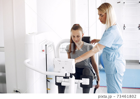 Young woman doing exercises on simulator with therapist in gym 73461802