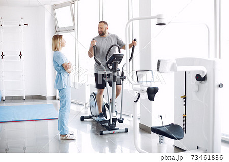 Patient doing exercise on spin bike in gym with therapist 73461836