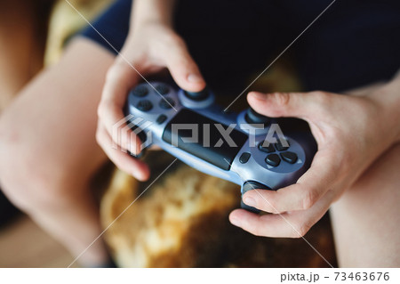 A teenager is sitting on the cofa and playing a A teenager is sitting on the cofa and playing a 73463676