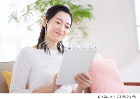 リビングでタブレットを操作するミドルの女性 リビングでタブレットを操作するミドルの女性 73465546