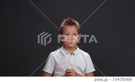 Expecting miracle boy in white shirt holding hands together in front of him while looking sideways at upper corner. Isolated on black background Expecting miracle boy in white shirt holding hands together in front of him while looking sideways at upper corner. Isolated on black background 73470569