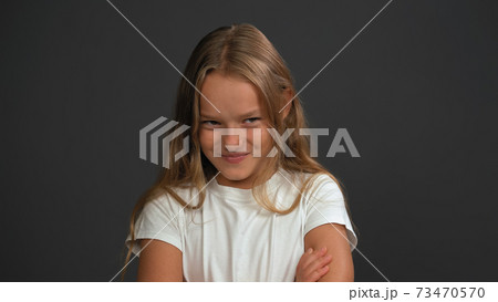 Close up. Little girl of 8,10 years with hands folded looks looks questioningly at the camera wearing white t shirt isolated on dark grey or black background 73470570