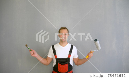 a handsome man in work overalls with a paint roller looking at the camera a handsome man in work overalls with a paint roller looking at the camera 73471652