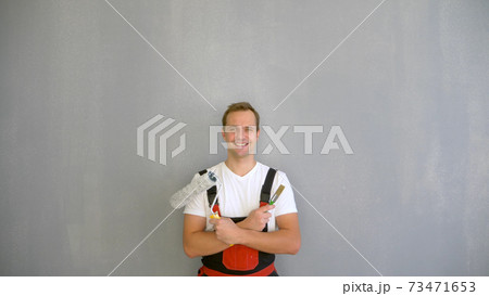 a handsome man in work overalls with a paint roller looking at the camera a handsome man in work overalls with a paint roller looking at the camera 73471653