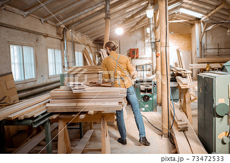 Carpenter carrying pine planks in the warehosue Carpenter carrying pine planks in the warehosue 73472533