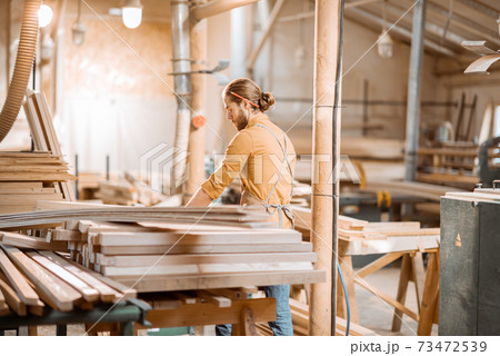 Carpenter carrying pine planks in the warehosue 73472539