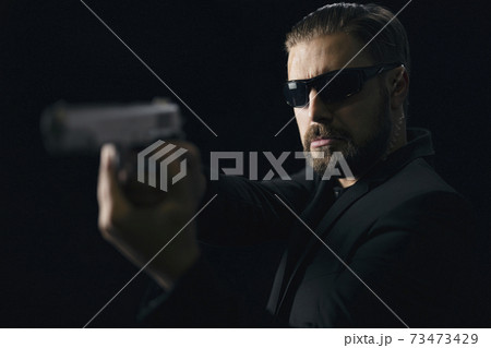 Bearded killer in sunglasses with gun in hands Bearded killer in sunglasses with gun in hands 73473429