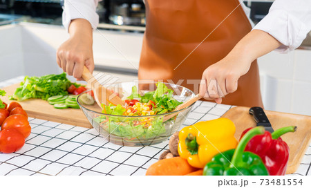 woman in the process of preparing healthy food Vegetable Salad mixing salad wooden spoon in kitchen at home Dieting Concept woman in the process of preparing healthy food Vegetable Salad mixing salad wooden spoon in kitchen at home Dieting Concept 73481554