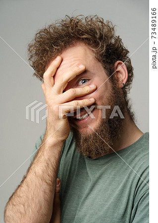 Shy handsome young man covered his face with hand pry with his eye, curly hair in olive t-shirt isolated on white background. Portrait of smiling young man Shy handsome young man covered his face with hand pry with his eye, curly hair in olive t-shirt isolated on white background. Portrait of smiling young man 73489166