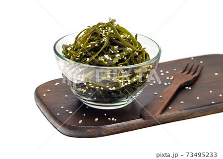 Seaweed kelp (Laminaria) in a glass bowl, sprinkle sesame seeds on a wooden board, Isolate on white background. Seaweed salad. Healthy food concept. Seaweed kelp (Laminaria) in a glass bowl, sprinkle sesame seeds on a wooden board, Isolate on white background. Seaweed salad. Healthy food concept. 73495233