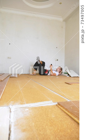 Builder in renovated room lying on floor using smartphone 73497005