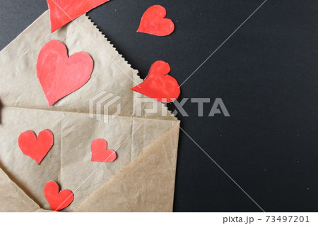 Red hearts drop out of crafting brown envelope on black background with a copy of the space 73497201