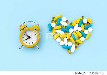 Medical pills in heart shape with alarm clock on blue background Medical pills in heart shape with alarm clock on blue background 73502569