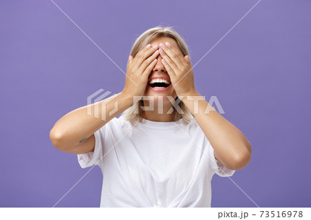 Can I look now. Portrait of excited pleased attractive tanned girlfriend in white t-shirt closing eyes and smiling broadly waiting for boyfriend bring surprising gift over purple background 73516978