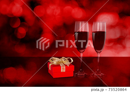 Two wineglasses and red gift box on desk with red blur bokeh background. 73520864