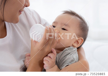 Young asian mother embracing and feeding little baby girl with bottle of milk at home. 73520865