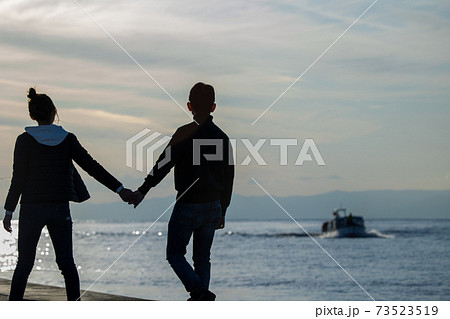 海を見つめて手をつないで歩くカップルの写真素材