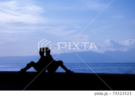 海沿いカップルの体操座り背中合わせシルエットの写真素材