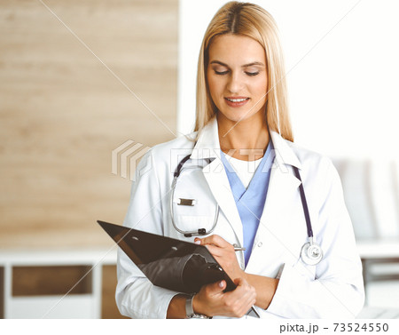 Doctor woman controls medication history records and exam results while using clipboard in sunny hospital . Medicine and healthcare concept 73524550