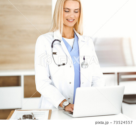 Woman-doctor controls medication history records and exam results while using laptop computer in sunny hospital. Medicine and healthcare concept Woman-doctor controls medication history records and exam results while using laptop computer in sunny hospital. Medicine and healthcare concept 73524557