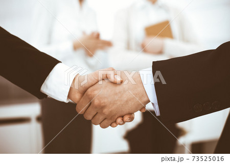 Businessman and woman shaking hands with colleagues at the background. Handshake at meeting in office. Concept of success in business 73525016