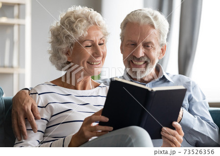 Happy bonding elderly senior retired family couple reading paper book. 73526356
