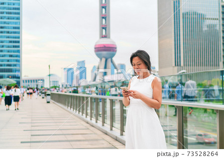 Phone Asian middle aged elegant woman using smartphone texting on Shanghai city street. Mature people lifestyle. Businesswoman holding mobile phone working. Smiling mature businesswoman in China Phone Asian middle aged elegant woman using smartphone texting on Shanghai city street. Mature people lifestyle. Businesswoman holding mobile phone working. Smiling mature businesswoman in China 73528264