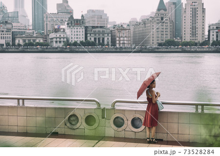 Shanghai city bund river Asian woman walking under rain with umbrella on China Asia vacation. Elegant chinese tourist lady in red dress 73528284