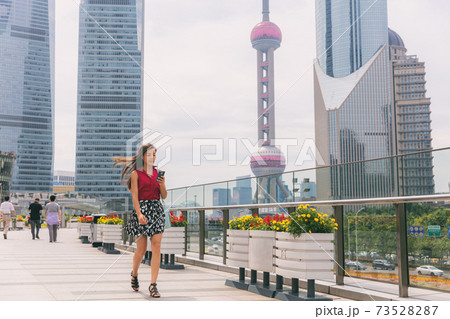Business woman walking using phone commuting to work in Shanghai city, China. Tourist travel lifestyle Asian lady city street walk, cityscape in summer. View of Pearl Tower during morning commute Business woman walking using phone commuting to work in Shanghai city, China. Tourist travel lifestyle Asian lady city street walk, cityscape in summer. View of Pearl Tower during morning commute 73528287