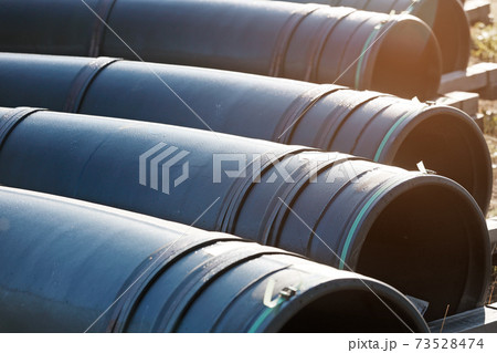 Large diameter black gasification pipes lie in a row in an open warehouse on the street on a summer Large diameter black gasification pipes lie in a row in an open warehouse on the street on a summer 73528474