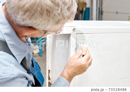 An employee paints metal products. An elderly man holds a foam sponge in his hand and paints the An employee paints metal products. An elderly man holds a foam sponge in his hand and paints the 73528486