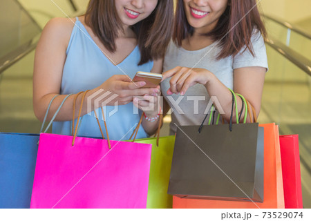Young girls holding shopping bag and checking online deal Young girls holding shopping bag and checking online deal 73529074