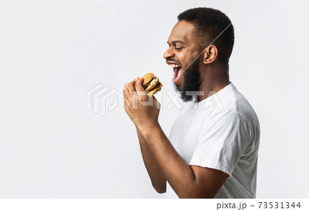 Side View Of Hungry Black Man Eating Burger, White Background Side View Of Hungry Black Man Eating Burger, White Background 73531344