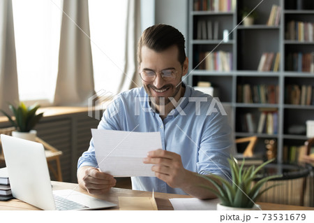 Smiling young businessman reading paper correspondence at home office. 73531679