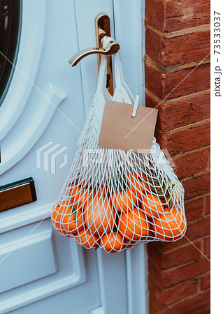 Reusable string bag from environmentally friendly materials with citrus fruits and blank card hanging on the door handle. Local farmer healthy food delivery. Zero-waste, plastic-free lifestyle. 73533037
