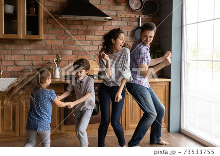 Overjoyed young family with kids dance in kitchen 73533755