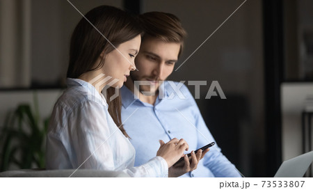 Close up colleagues using phone together, enjoying break in office 73533807
