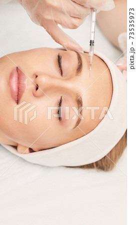 Forehead injection at spa salon. Doctor hands. Pretty female patient. 73535973