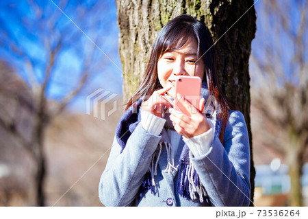 旅行先の公園で日差しが強い中スマホを使う女性 旅行先の公園で日差しが強い中スマホを使う女性 73536264