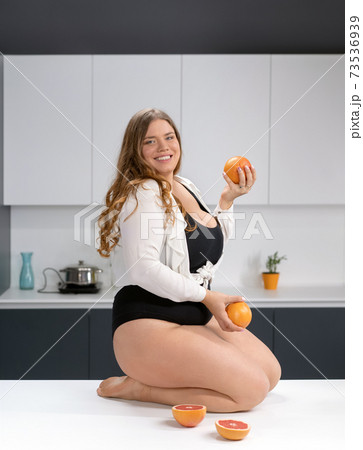 Healthy food happy curvy body young woman with long blond hair juggling fruits sitting on modern kitchen table, blending fresh fruits for healthy smoothie. Dieting and nutrition concept Healthy food happy curvy body young woman with long blond hair juggling fruits sitting on modern kitchen table, blending fresh fruits for healthy smoothie. Dieting and nutrition concept 73536939