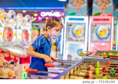 Little blond boy wearing a medical mask during COVID-19 coronavirus playing board table soccer 73540194