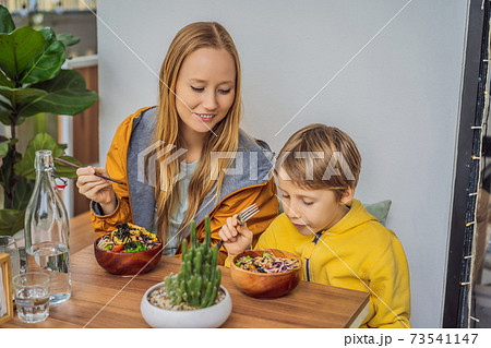 Mother and son eating Raw Organic Poke Bowl with Rice and Veggies close-up on the table. Top view from above horizontal 73541147