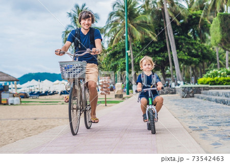 Happy family is riding bikes outdoors and smiling. Father on a bike and son on a balancebike Happy family is riding bikes outdoors and smiling. Father on a bike and son on a balancebike 73542463