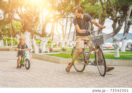 Happy family is riding bikes outdoors and smiling. Father on a bike and son on a balancebike 73542501