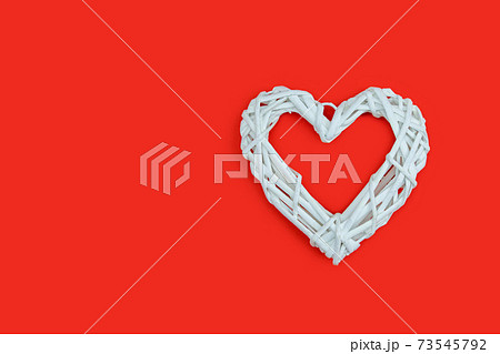 White wicker heart symbol lies on the red background to Valentine's Day. Top view. Flat lay. Greeting card, concept of the holiday of lovers. 73545792