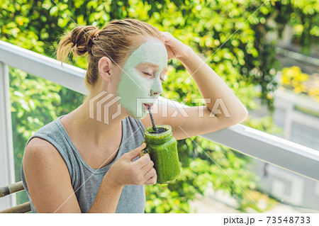 Spa Woman applying Facial green clay Mask. Beauty Treatments. Fresh green smoothie with banana and spinach with heart of sesame seeds. Love for a healthy raw food concept. Detox Concept Spa Woman applying Facial green clay Mask. Beauty Treatments. Fresh green smoothie with banana and spinach with heart of sesame seeds. Love for a healthy raw food concept. Detox Concept 73548733