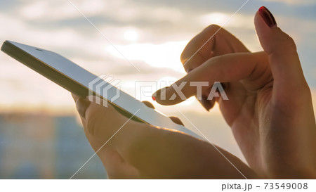 Woman using smartphone against warm sunset sky: close up side view 73549008